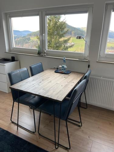 a wooden table and chairs in a room with two windows at Studio Tonbachblick Baiersbronn in Baiersbronn