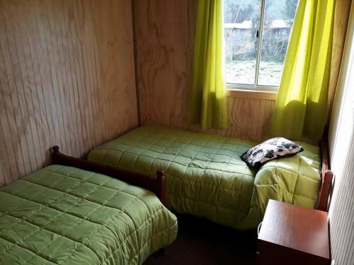 Habitación con 2 camas y ventana con cortinas amarillas. en Cabañas Amanecer, en Riñinahue