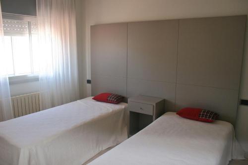 Habitación con 2 camas, sábanas blancas y almohadas rojas. en Apartamentos Angelito Playa América, en Nigrán