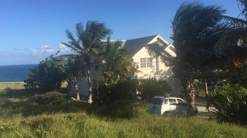 a white house with palm trees and a white car at Oceanfront 2 bedroom apartment in Saint Philip