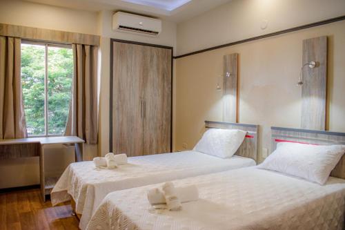 a bedroom with two beds with white sheets and a window at Hotel Rio Dorado in Encarnación