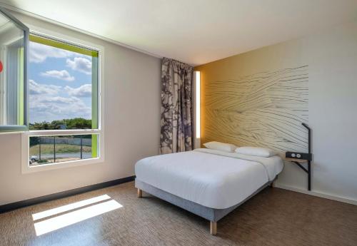 a bedroom with a bed and a large window at B&B HOTEL Saintes in Saintes