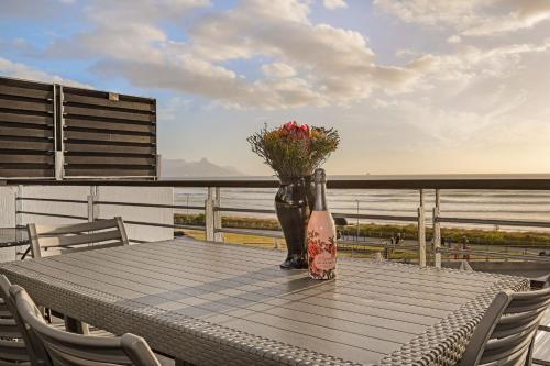 a table with a vase with flowers on a balcony at Eden on the Bay 167 by HostAgents in Bloubergstrand