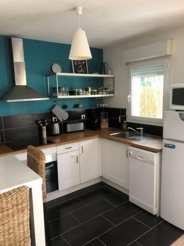 une cuisine avec des armoires blanches et un mur bleu dans l'établissement Appartement T2 calme absolu, large terrasse, garage vélo, 5 min océan, à Anglet