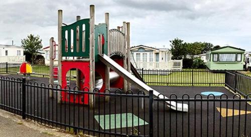 a small playground with a slide in front of a fence at Caravan 521 shuker in Talybont