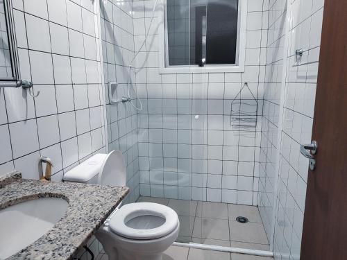 a white tiled bathroom with a toilet and a sink at Apartamento no Centro de Ubatuba in Ubatuba