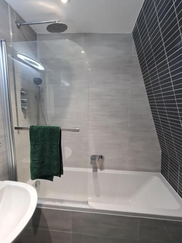 ein Badezimmer mit einer Badewanne, einem Waschbecken und einem grünen Handtuch in der Unterkunft 20 mins to central London, Stylish sky views 2 bed in London