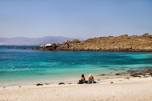two people sitting on a beach near the water at cabañas de la casona in Punta de Choros