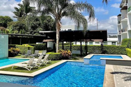 una piscina con sillas y una palmera y un edificio en Condo Tranquilo, Cómodo y Moderno en Santa Ana, en Santa Ana