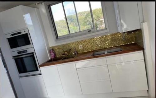 une cuisine avec des armoires blanches et une fenêtre dans l'établissement T4 morgiou/prado, à Marseille