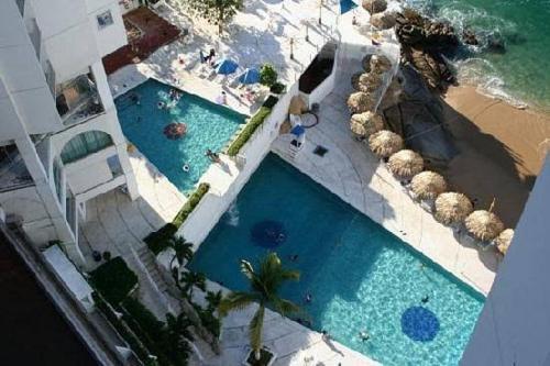 una vista aérea de 2 piscinas junto a la playa en departamento con vista al mar en Acapulco