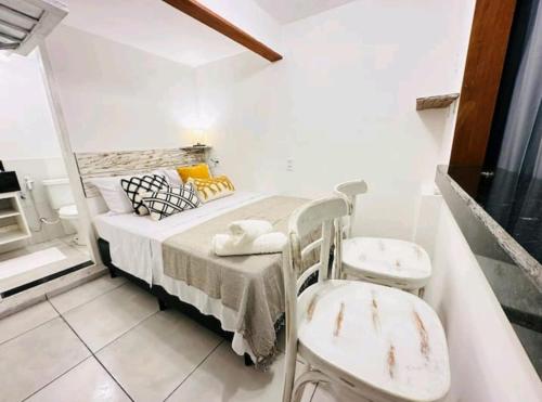 a small bedroom with a bed and two chairs at Apartamentos Charmosos na Avenida Principal de Buzios in Búzios