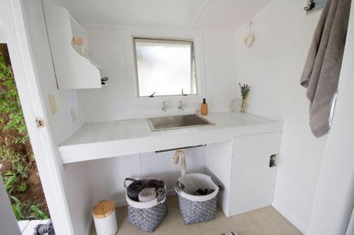 uma cozinha branca com um lavatório e duas latas de lixo em The Cowshed em Whitianga