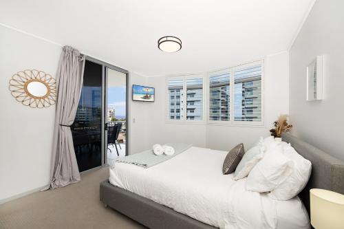 a white bedroom with a bed and a balcony at Suttons Cove in Redcliffe