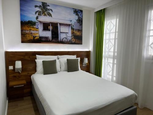 ein Schlafzimmer mit einem weißen Bett und einem Gemälde an der Wand in der Unterkunft Hôtel Exsel Créolia in Saint-Denis