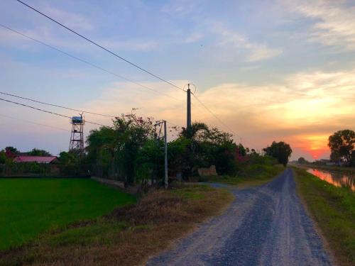 a dirt road with the sunset in the background at LA'S FARMSTAY in Trảng Bàng