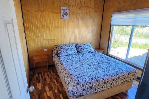 a bedroom with a bed with a blue comforter and a window at Cabaña buck in Dalcahue