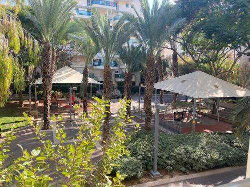 a park with palm trees and umbrellas and a building at Beach Apartment - Ramat Aviv in Tel Aviv