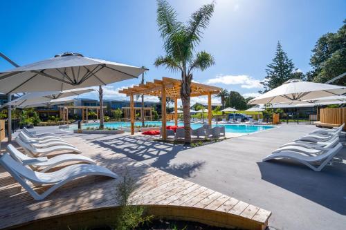 a group of chairs and umbrellas next to a pool at Tasman Holiday Parks - Papamoa Beach in Papamoa