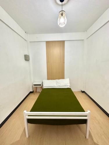 um quarto branco com uma cama com um cobertor verde em Zz Dormitel em Nabua