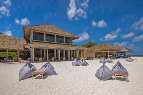 a group of chairs on the beach in front of a building at Emerald Faarufushi Resort & Spa - Deluxe All Inclusive in Raa Atoll