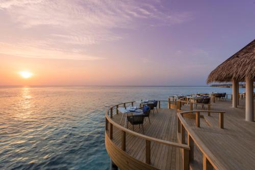 a restaurant on the water with the sun setting at Emerald Faarufushi Resort & Spa - Deluxe All Inclusive in Raa Atoll