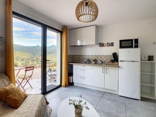 Il comprend une cuisine équipée d'un réfrigérateur blanc, d'une table et d'une fenêtre. dans l'établissement Joli Studio au cœur du maquis, à Ocana