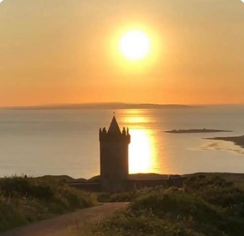 a sunset over the ocean with a lighthouse at An Caban Ciuin in Doolin