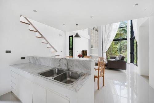 eine weiße Küche mit einem Waschbecken und ein Wohnzimmer in der Unterkunft Ana's House in Nathon Bay