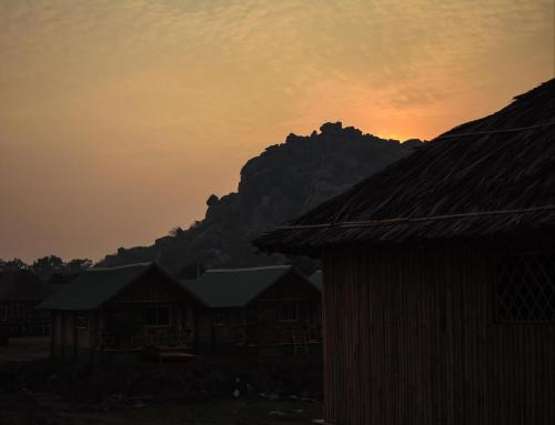 a sunset over houses with a mountain in the background at Mowgli's Cafe Hampi & Guest House in Hampi