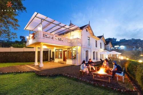 a group of people sitting around a fire in front of a house at Zostel Ooty in Ooty