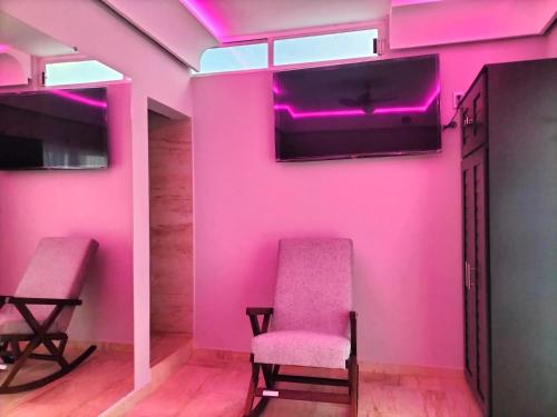 Zimmer mit rosa Wänden, 2 Stühlen und einem TV in der Unterkunft AMG in Tehuacán