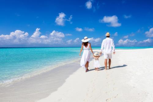 a man and a woman and child walking on the beach at Emerald Faarufushi Resort & Spa - Deluxe All Inclusive in Raa Atoll