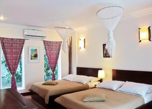 two beds in a room with red drapes at Sabbay Kep in Kep