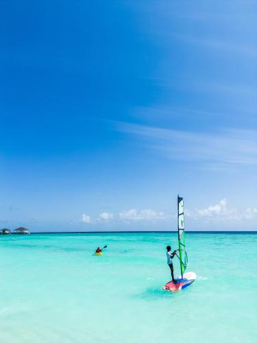 a person on a surfboard with a sail in the ocean at ROBINSON NOONU - All Inclusive in Manadhoo
