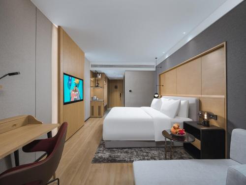 a hotel room with a large white bed and a desk at Park Inn by Radisson Tianjin Five Old Street Nanjing Road in Tianjin