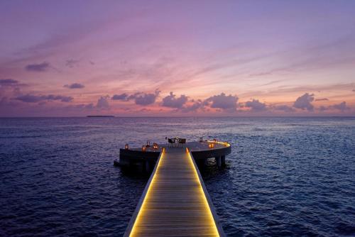 a dock in the middle of the ocean at sunset at Emerald Faarufushi Resort & Spa - Deluxe All Inclusive in Raa Atoll
