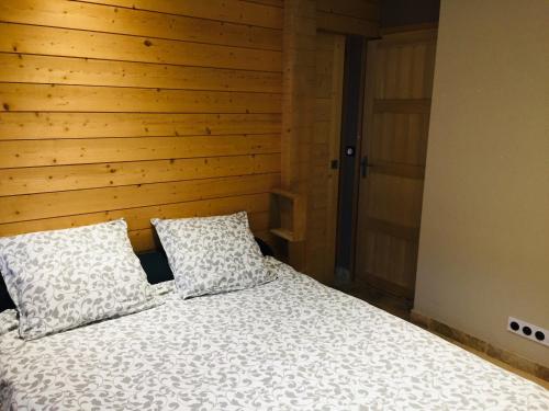 ein Bett mit zwei Kissen in einem Schlafzimmer mit einer Holzwand in der Unterkunft Le Séchoir un Grand coin de paradis in Saint-Amand-de-Coly