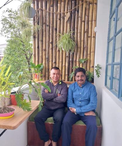 two men sitting on a bench in a room with plants at Vilasa Homestay in Darjeeling