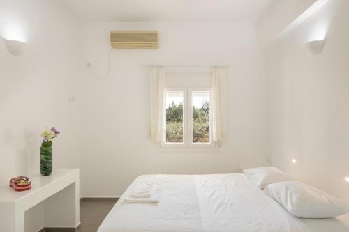 a white bedroom with a bed and a window at Andriana's cycladic house close to the sea in Drios