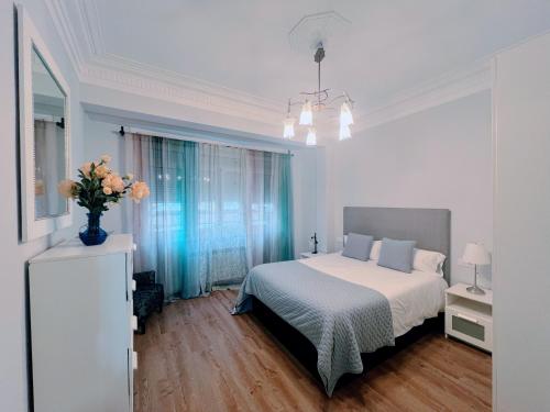 a white bedroom with a bed and a vase of flowers at Céntrico piso con patio y garaje in A Coruña