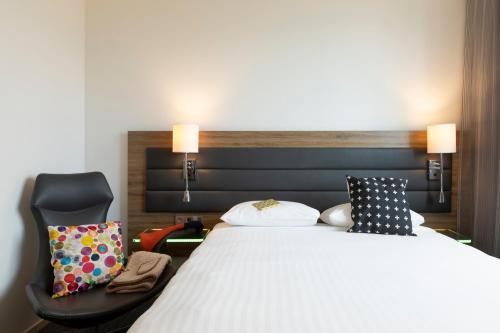 um quarto com uma cama grande e uma cadeira em Moxy Paris Charles de Gaulle Airport em Roissy-en-France