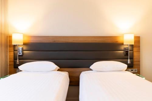 two beds in a hotel room with white sheets at Moxy Paris Charles de Gaulle Airport in Roissy-en-France