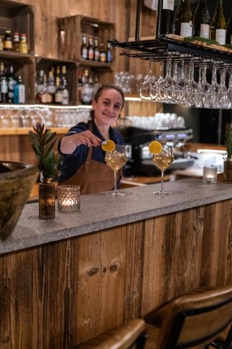 un homme debout derrière un bar avec deux verres à vin dans l'établissement Dormio Resort Les Portes du Grand Massif, à Flaine
