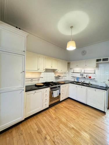 a large kitchen with white cabinets and a wooden floor at Spacious 4BD Family Home with GardenKensal Green! in London