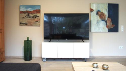 a living room with a tv on a wall with paintings at Wohnung mit Sauna, Garten & Schwimmteich in Bietigheim-Bissingen