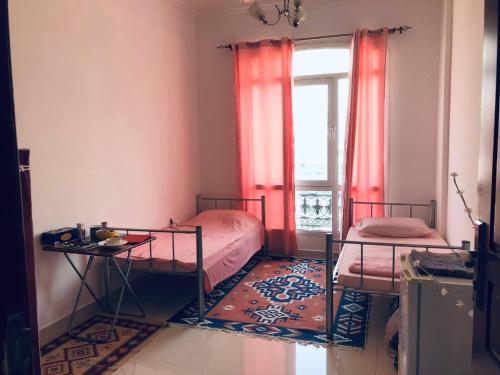 1 dormitorio con 2 camas y una ventana con cortinas rojas en Muscat Hostel 2300, en Mascate
