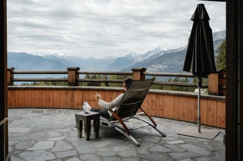 a man sitting in a chair on a patio with an umbrella at LeCrans in Crans-Montana
