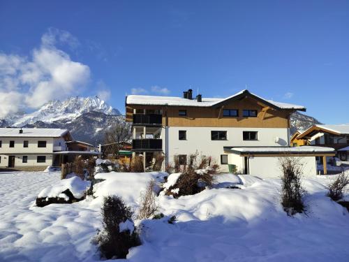 uma casa na neve com montanhas ao fundo em Ferienwohnung Ortner em Sankt Johann in Tirol