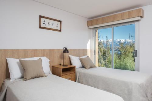 two beds in a room with a window at Bahía Montaña Resort in Villa La Angostura